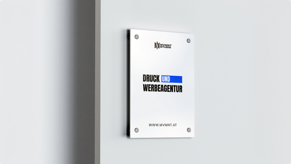Metal wall plaque advertising 'DRUCK UND WERBEAGENTUR' with a blue bar under 'UND', MV MNT STUDIO logo at the top, and the website www.mvmnt.at