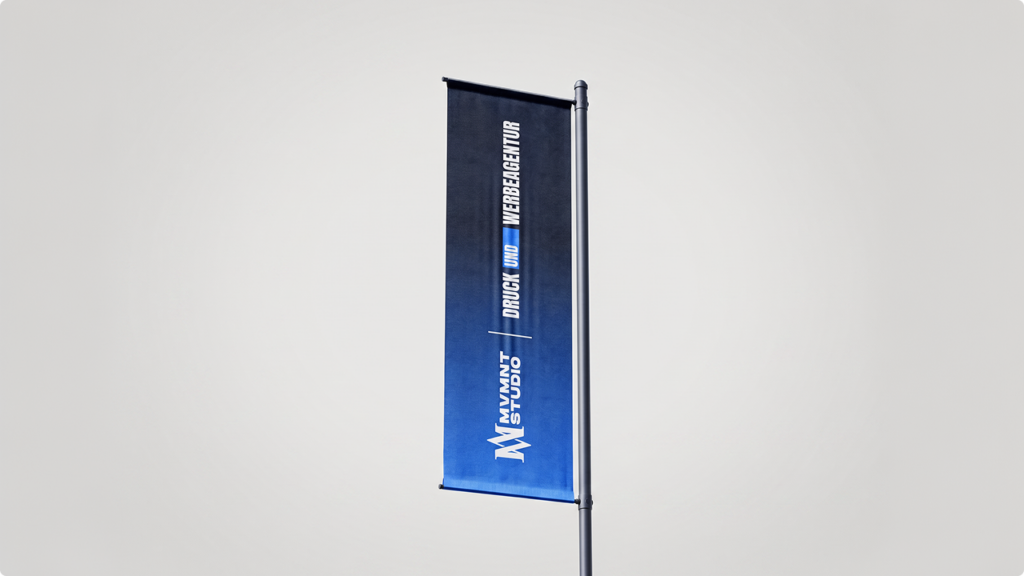 Vertical blue gradient advertising banner mounted on a metal pole, featuring a white logo and German text for a design/advertising studio