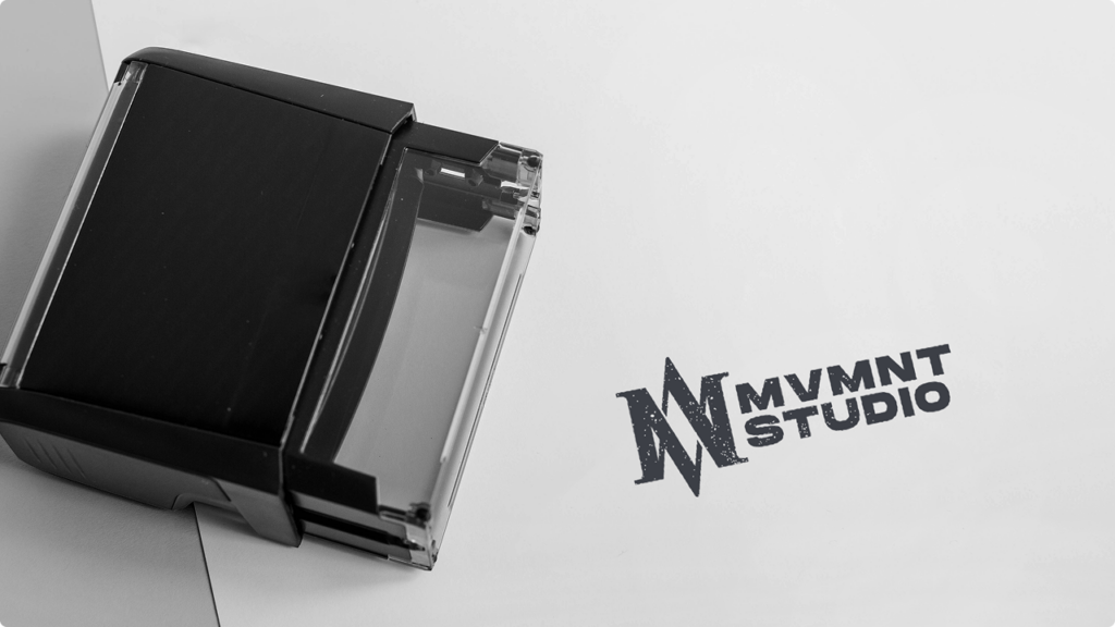 Black desktop stamp on a light surface beside a bold MVMNT STUDIO logo impression on paper.