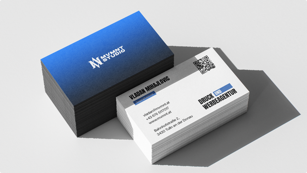Stacks of business cards on a light surface; blue gradient card with a logo beside a white card showing a name, contact details, and a QR code.